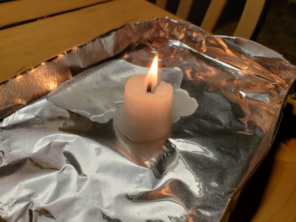 A squat white candle burning on a metal surface.