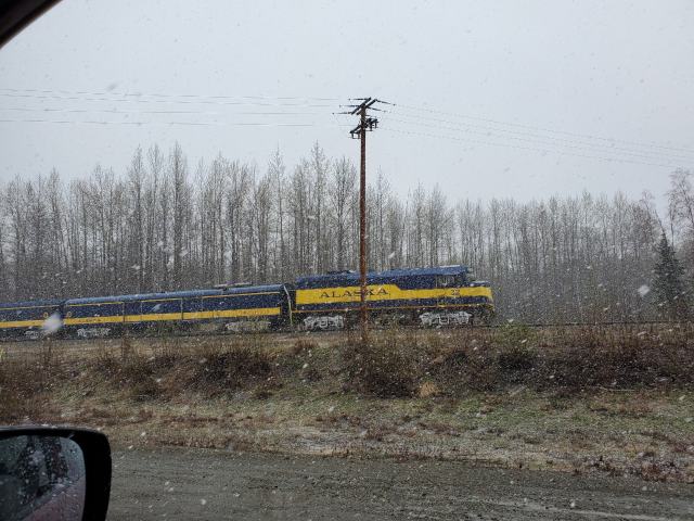 a blue and yellow train with falling snow, taken out of a car window